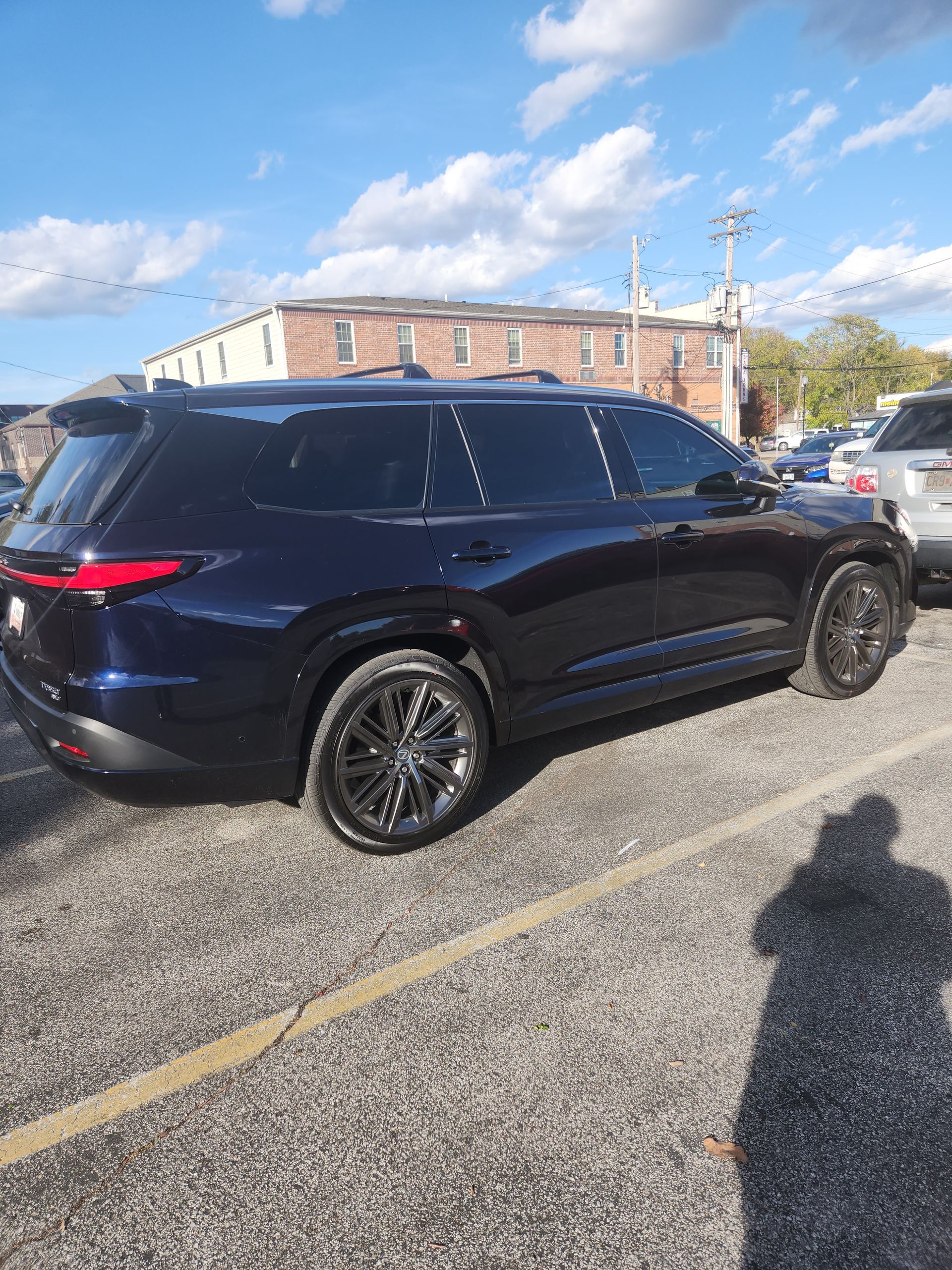 Black SUV parked in a lot under a partly cloudy sky, with a brick building in the background.