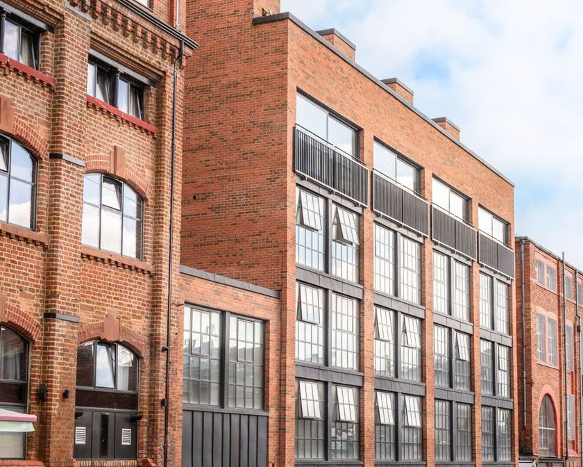 Red brick industrial buildings with large windows along a street under a cloudy sky