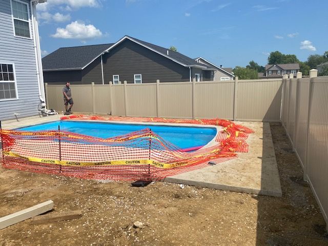A man is standing in front of a fence next to a swimming pool.