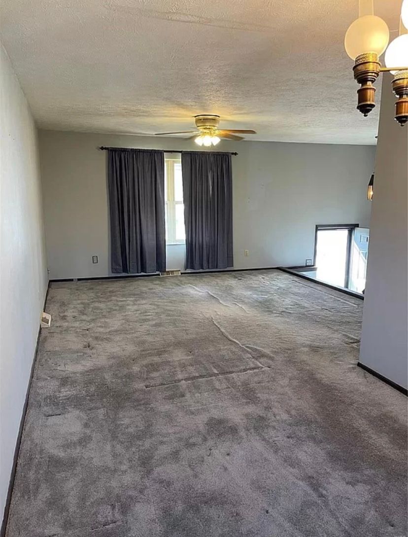 An empty living room with a ceiling fan and curtains.