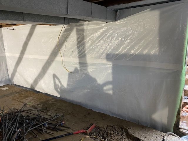 A shadow of a shovel is cast on a wall covered in plastic.