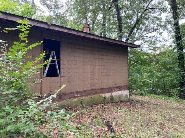 A small brown house with a ladder in front of it in the woods.