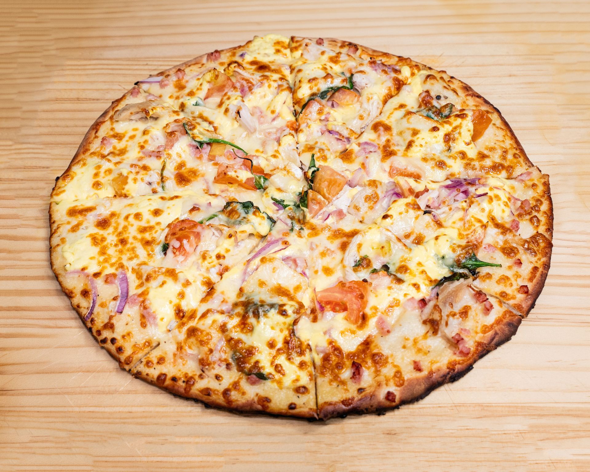 Pizza with melted cheese, red onion, and spinach on a wooden table.