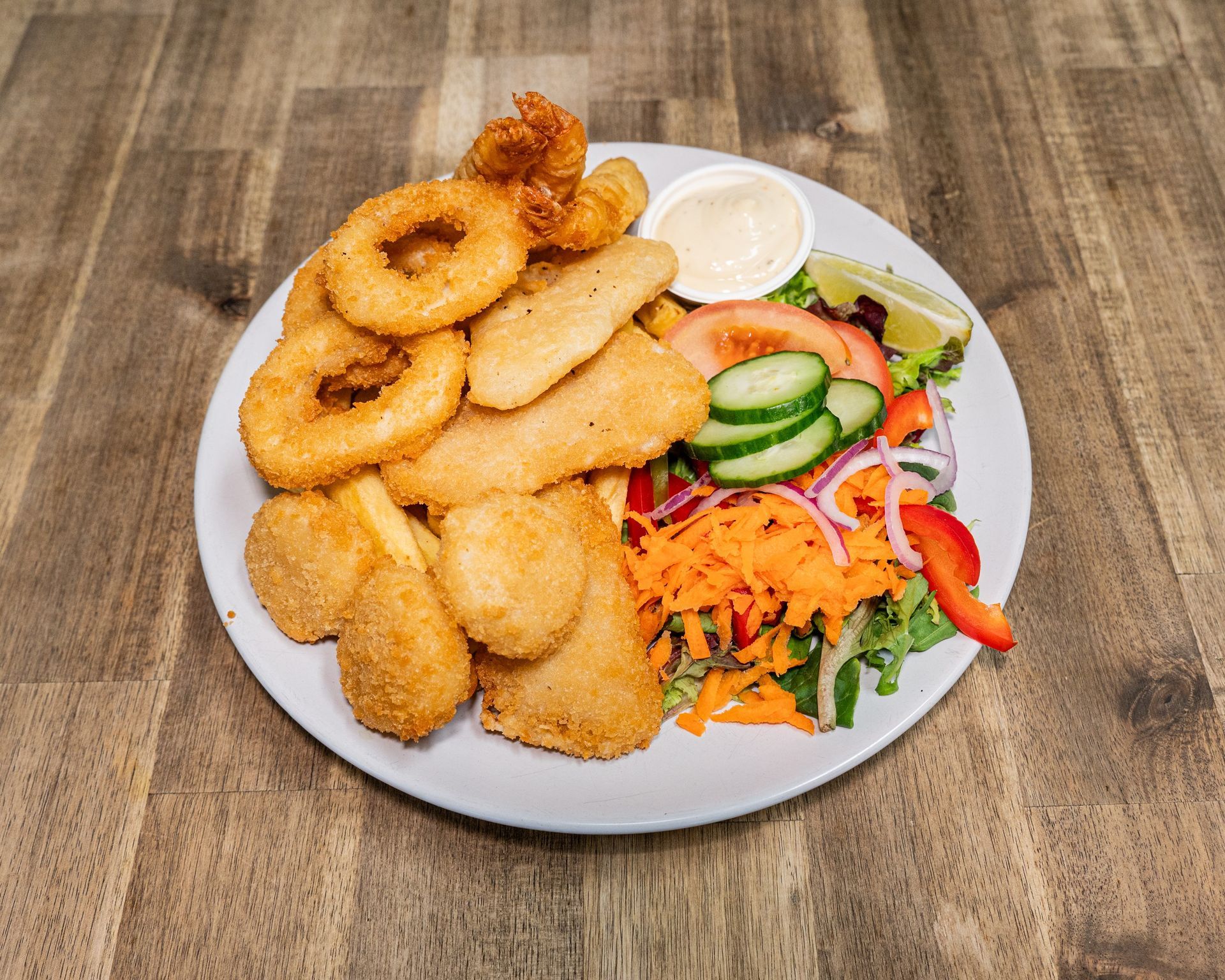 Plate with fried seafood, fries, salad, and sauce on a wooden table.