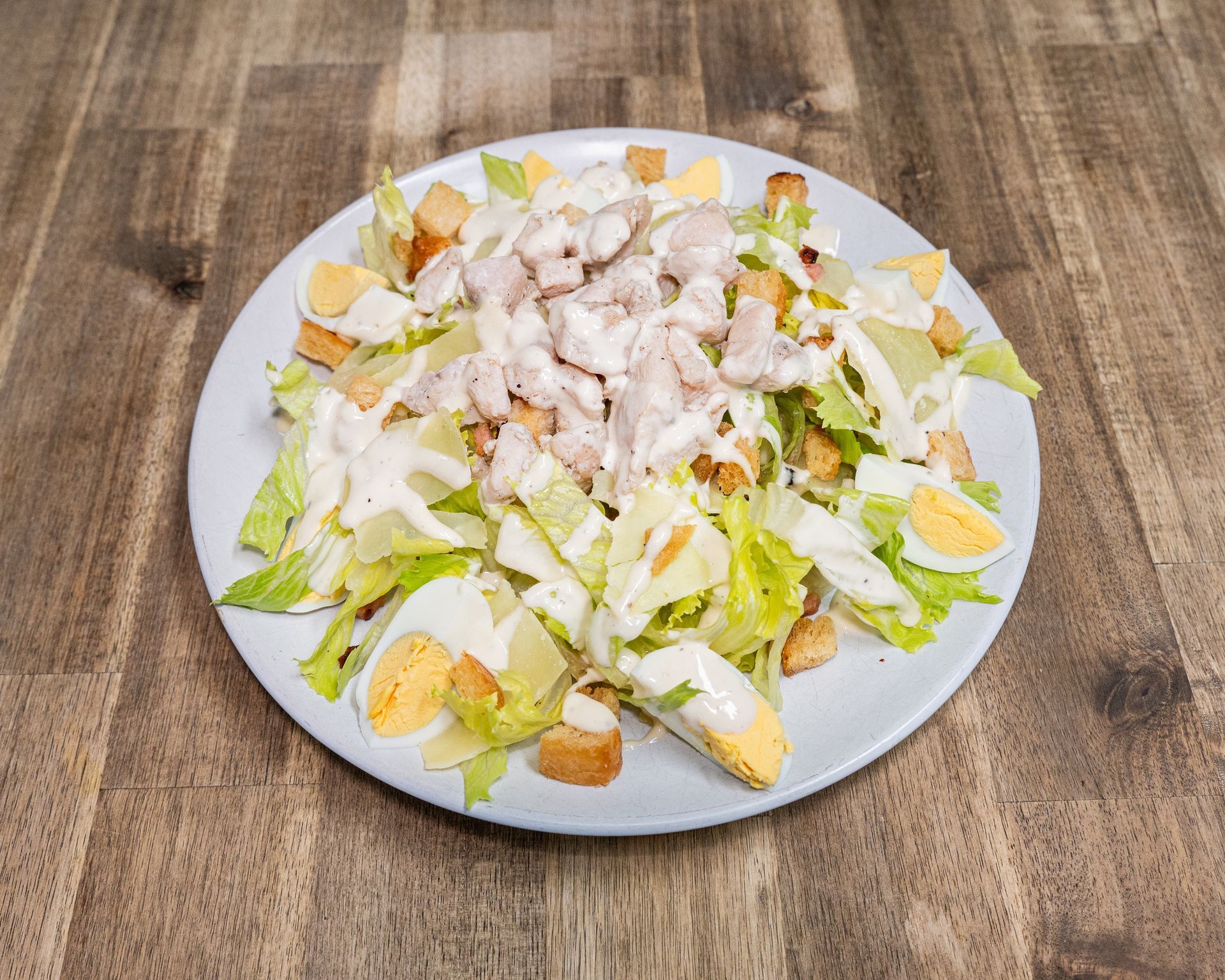 Caesar salad on a plate: romaine lettuce, croutons, chicken, boiled eggs, and creamy dressing.