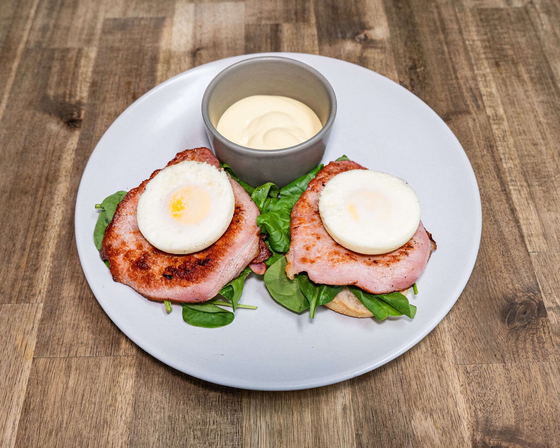 Two eggs benedict with hollandaise sauce on a plate, wooden table.