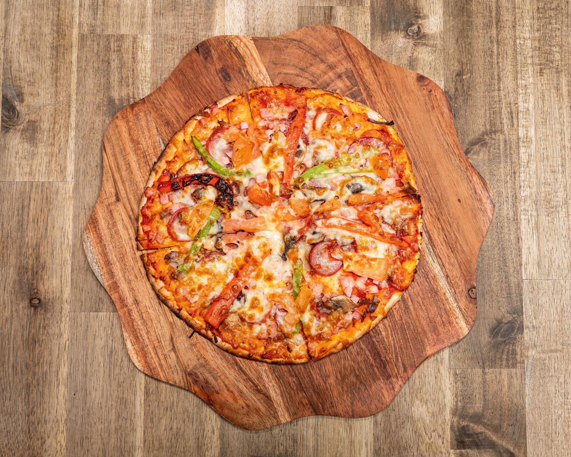 Pizza on a wooden serving board, sliced and topped with vegetables and cheese.