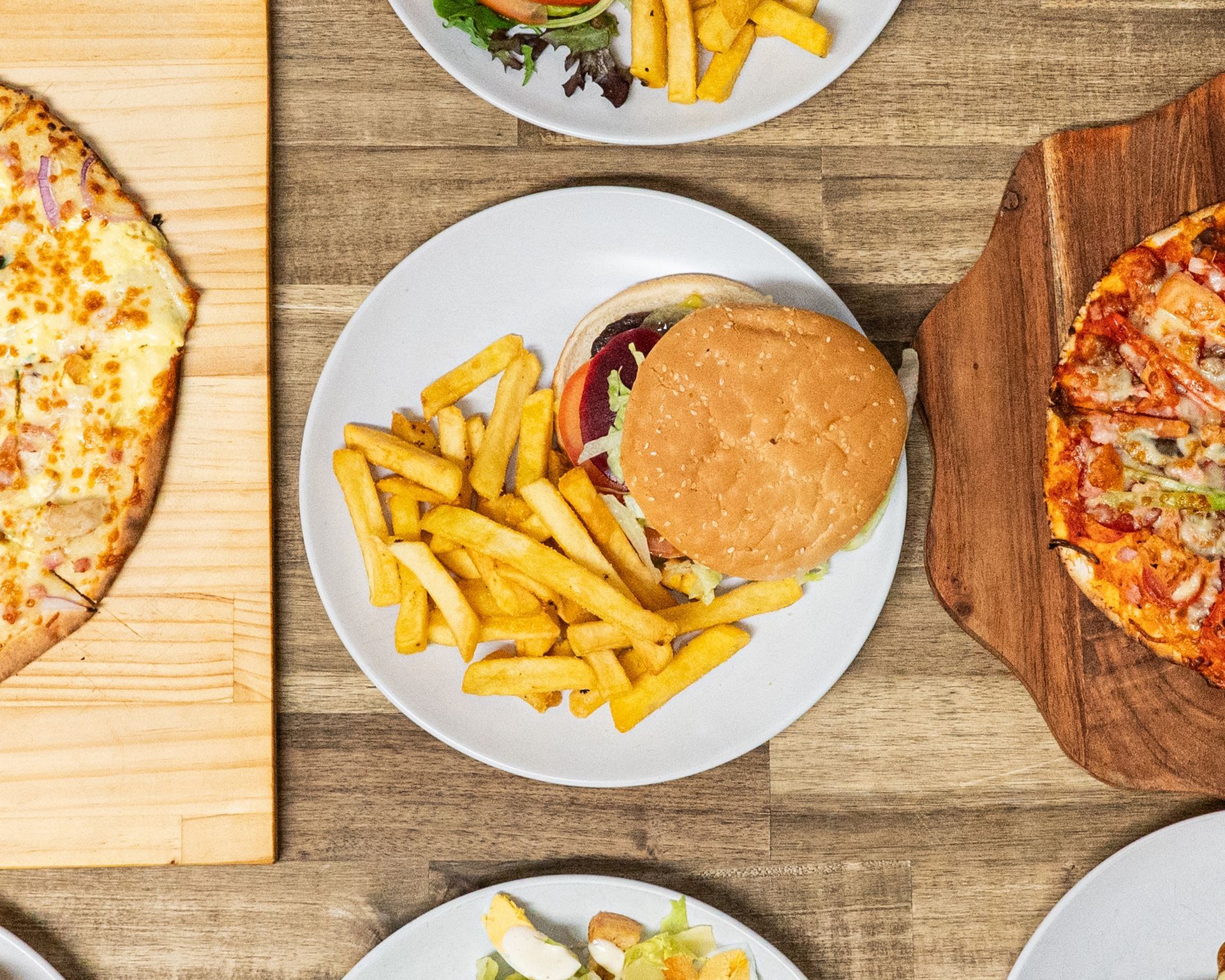 Chicken parmigiana with fries, salad, and tomato on a white plate atop a wooden table.