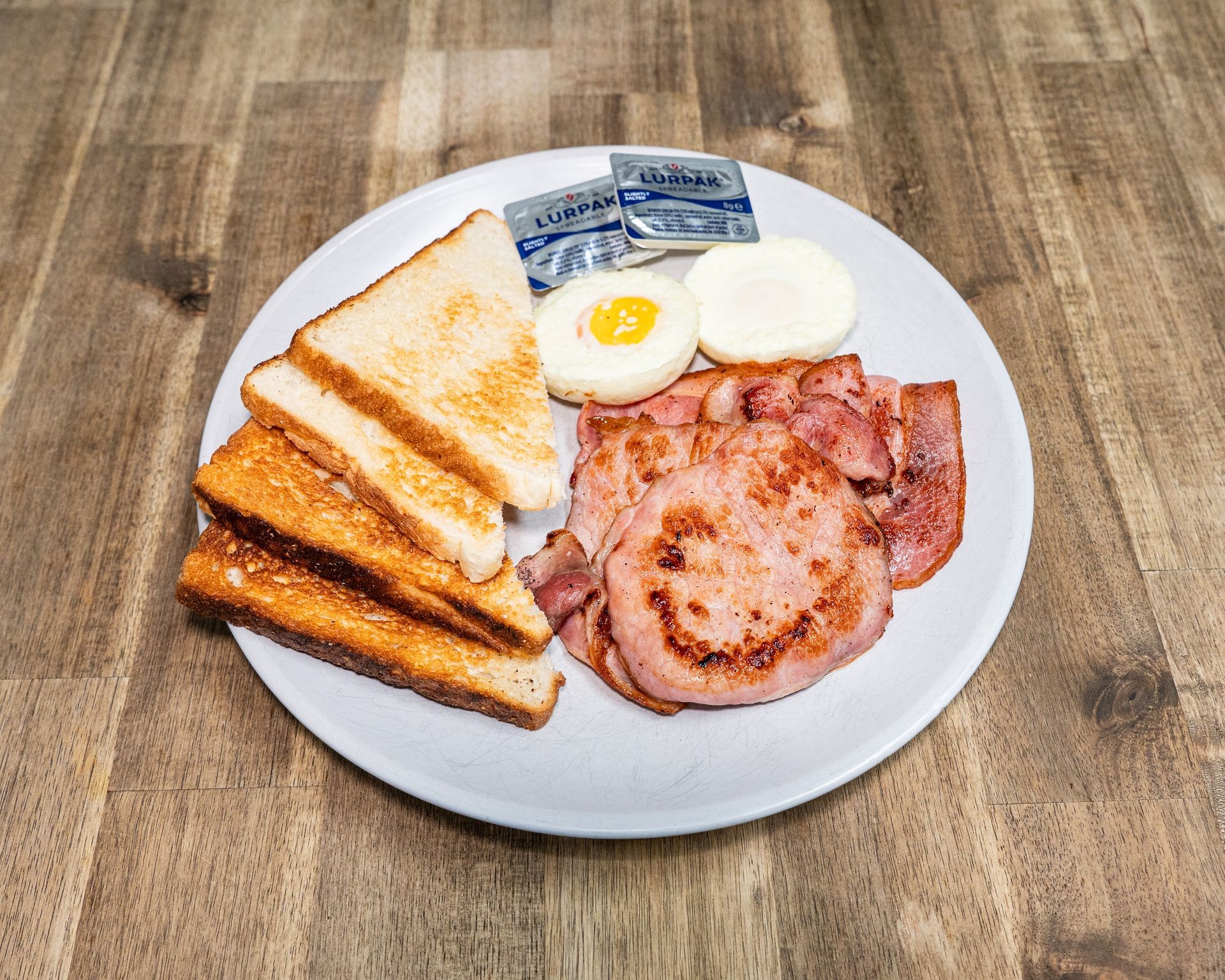 Plate of breakfast food: toast, eggs, bacon, butter packets.