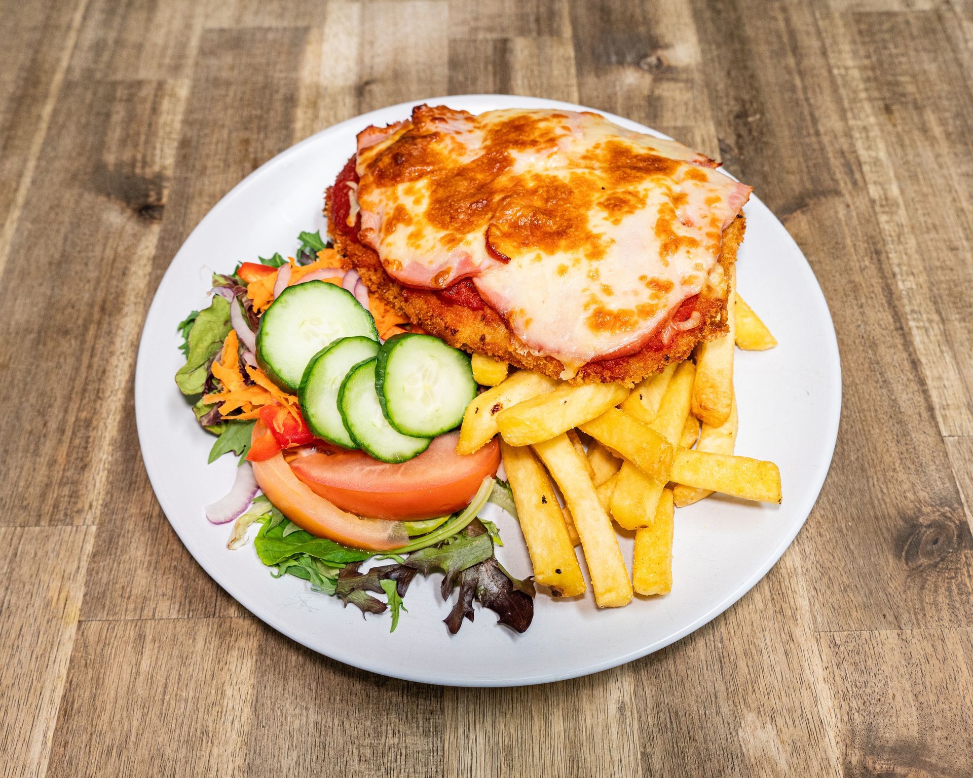 Chicken parmigiana with fries and salad on a white plate.