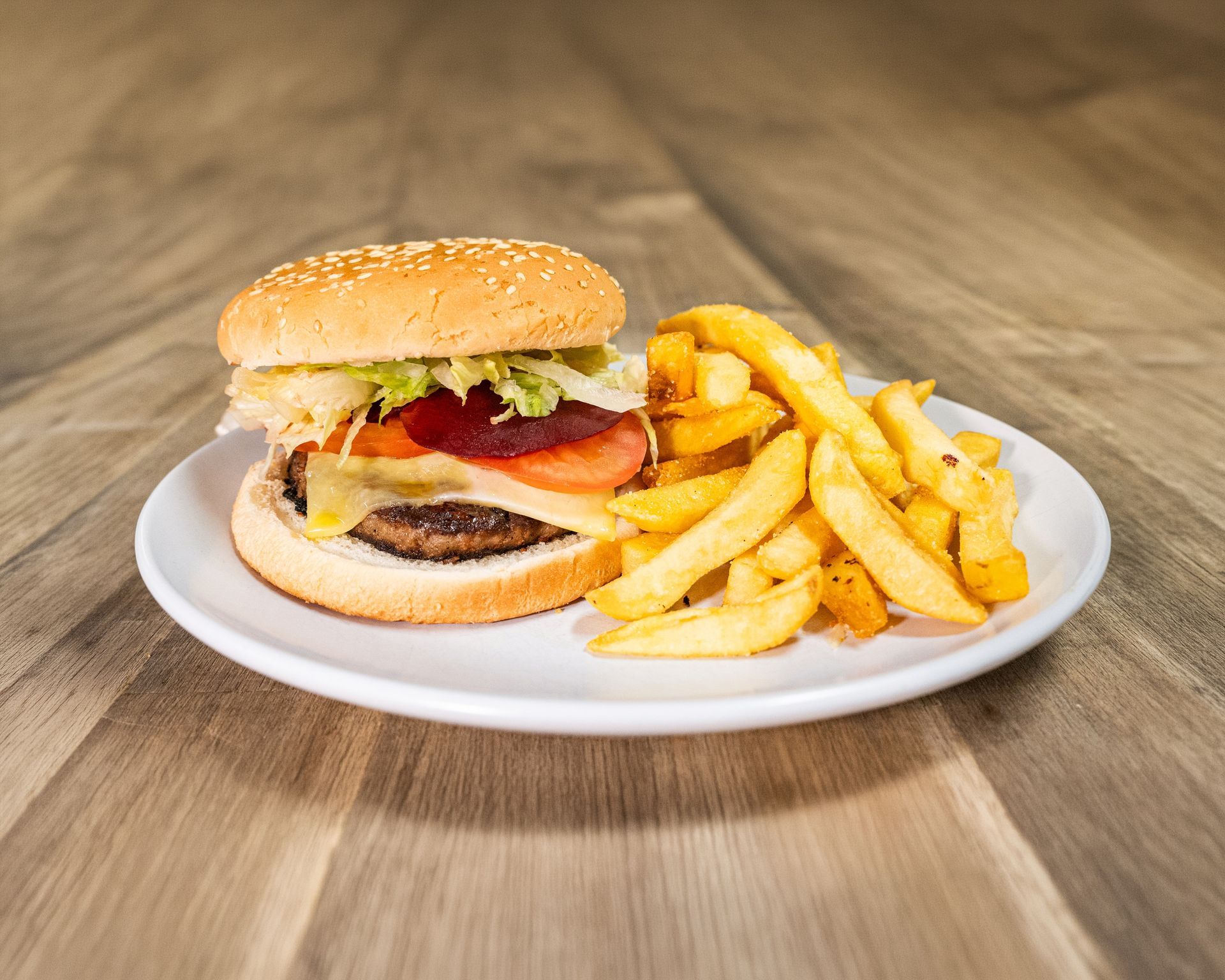 Burger with fries on a white plate, set on a wooden table.