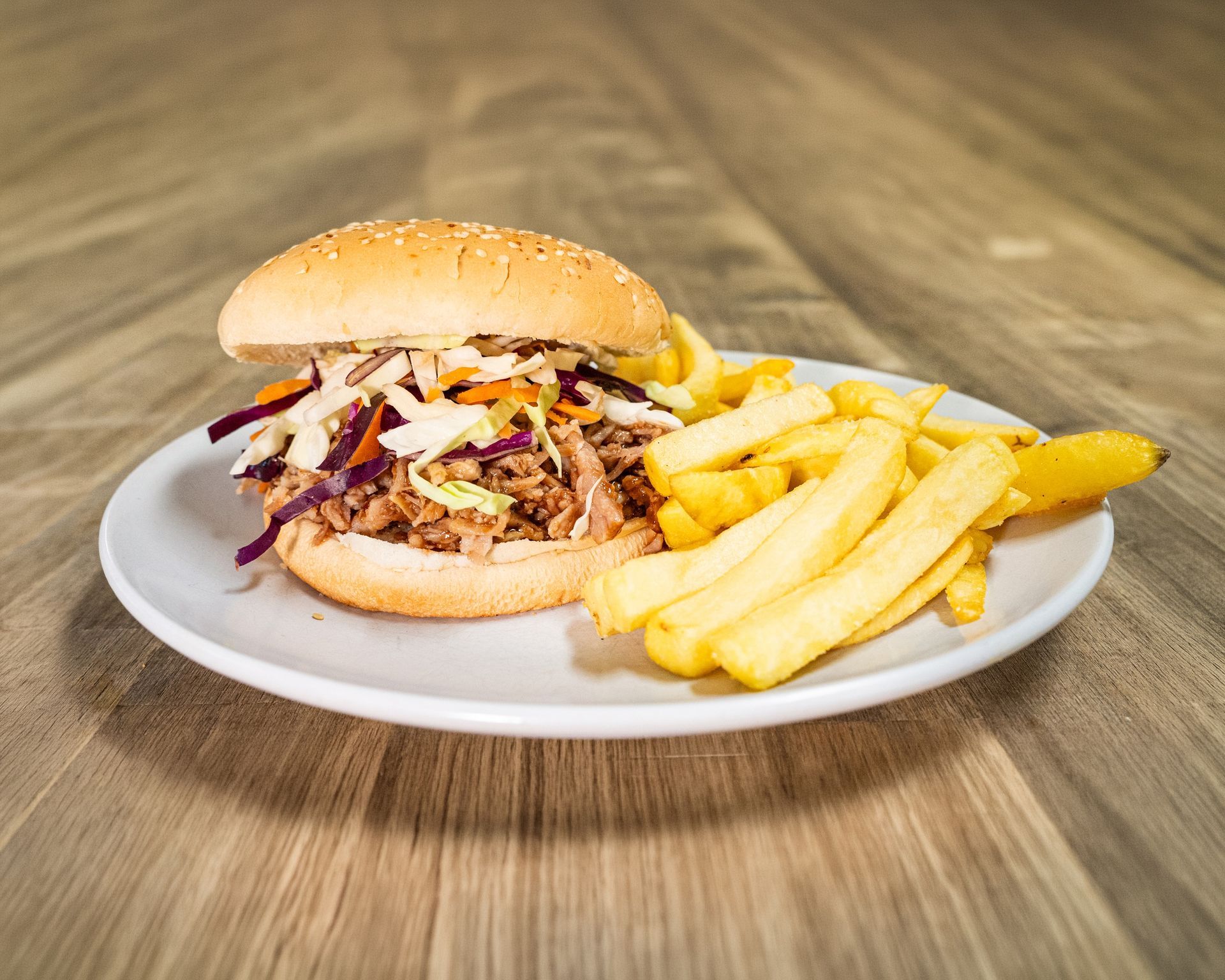 Pulled pork sandwich with coleslaw and fries on a white plate.