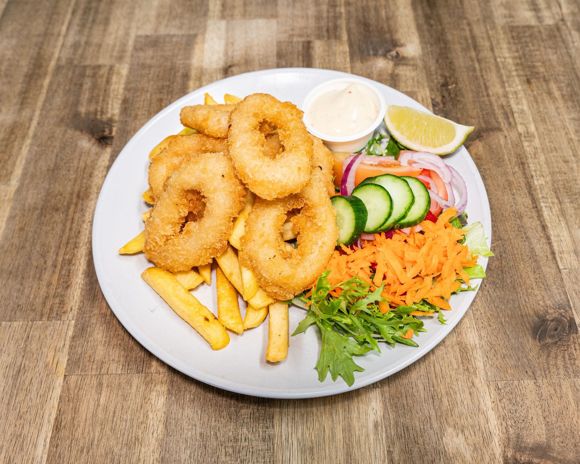 Plate of fried calamari rings, fries, salad, sauce, and lemon slice.