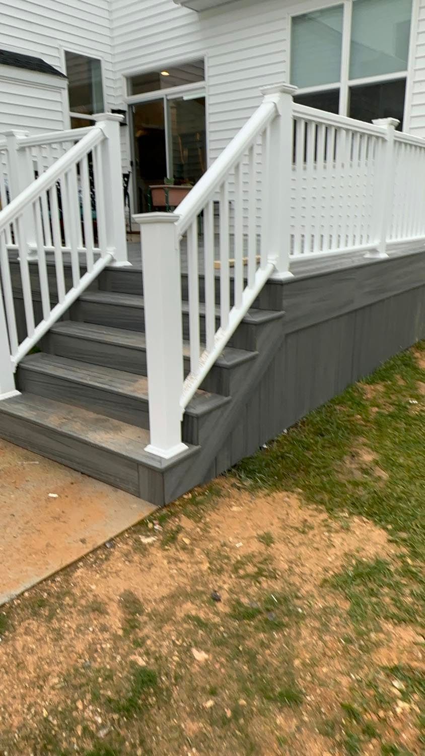 A deck with stairs and a white railing in front of a house.