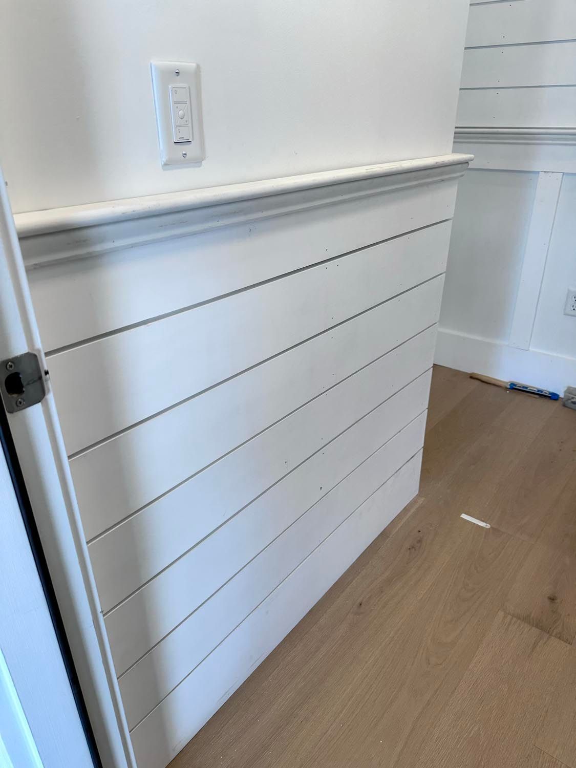 A white wall with wood paneling and a light switch on it.