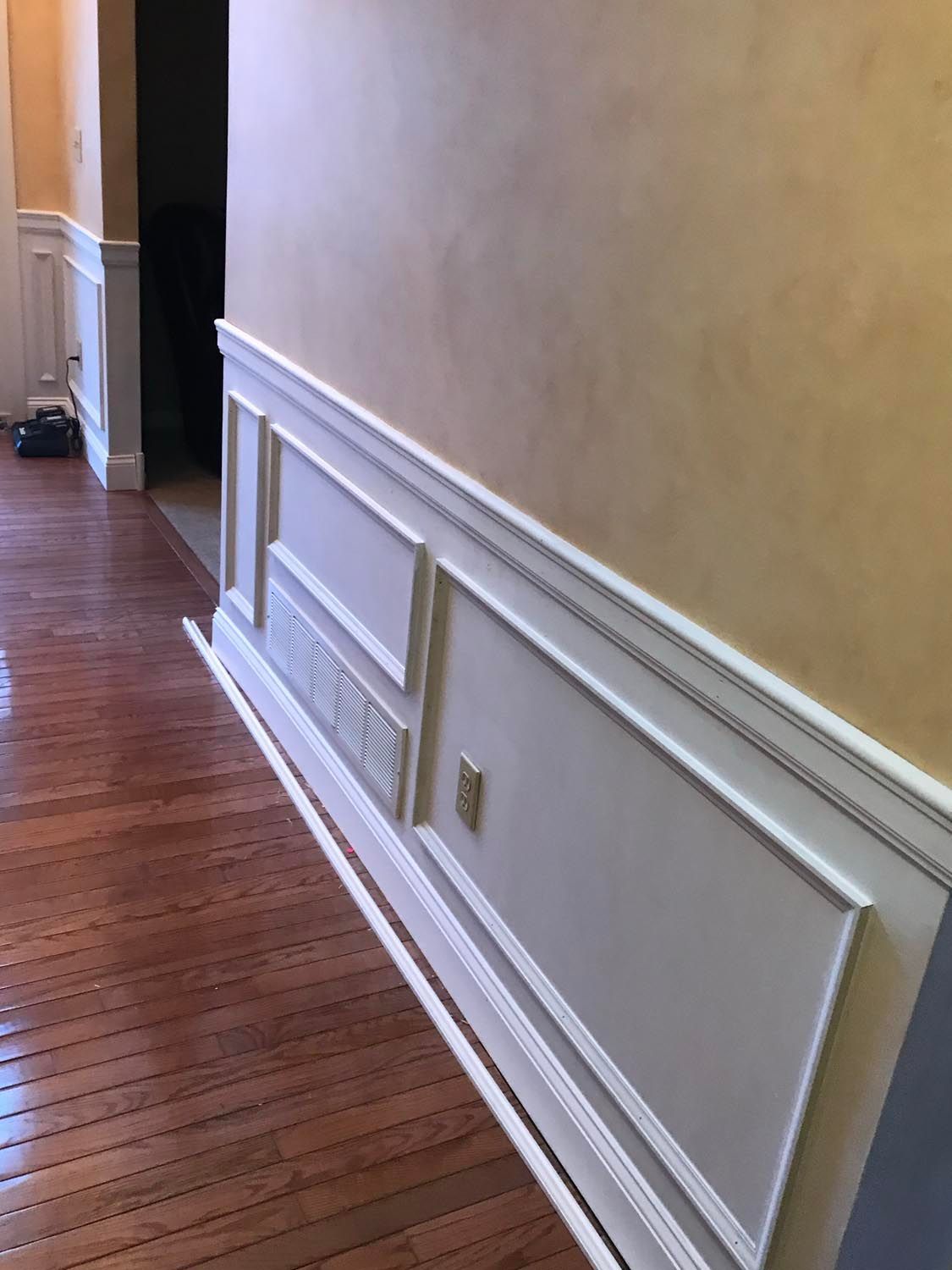 A hallway with hardwood floors and white trim on the walls.