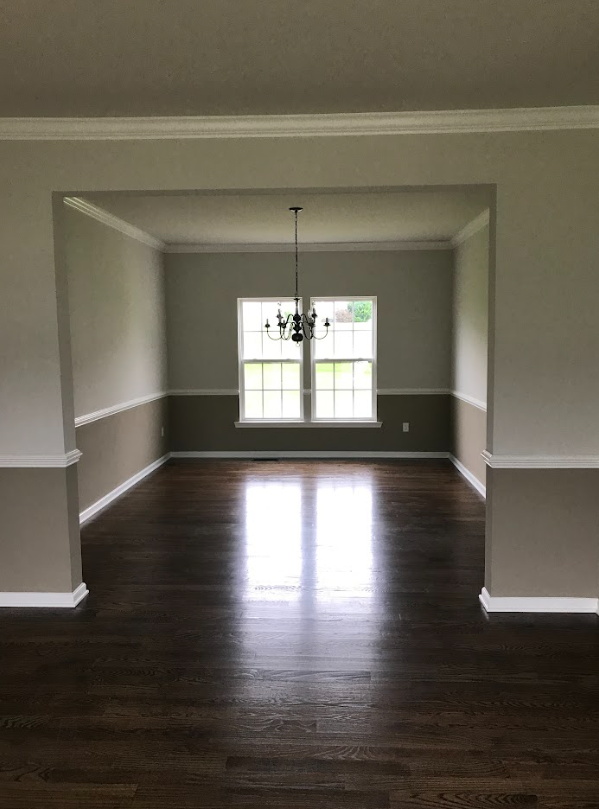 An empty dining room with hardwood floors and a chandelier hanging from the ceiling.