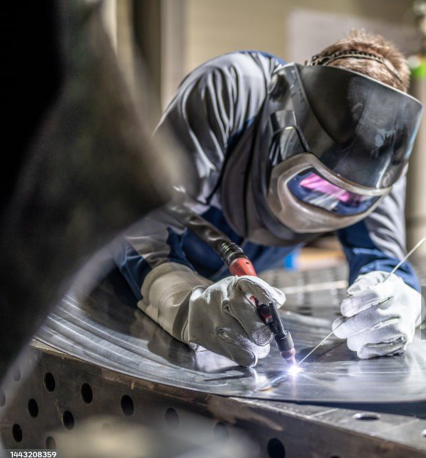 Welder in protective gear using a torch on a metal surface, creating a bright spark.