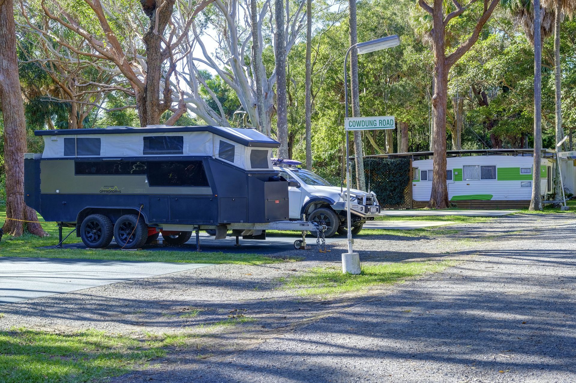 Caravan trailer and SUV parked at a campsite, street sign visible.— Pacific Palms Caravan Park in Elizabeth Beach, NSW