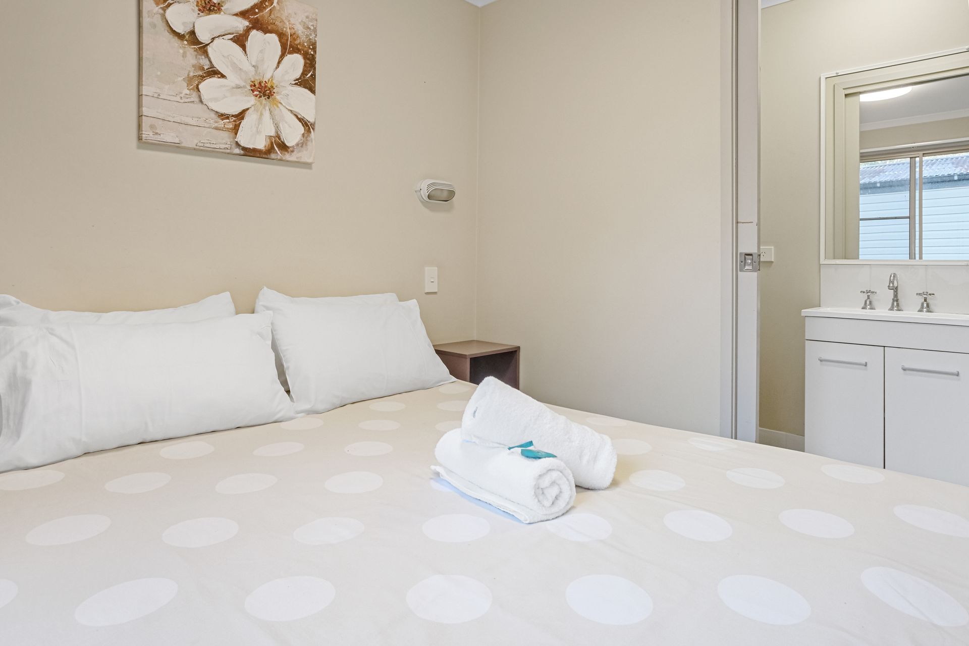 Bedroom with bed, towels, painting, and a bathroom door.— Pacific Palms Caravan Park in Elizabeth Beach, NSW