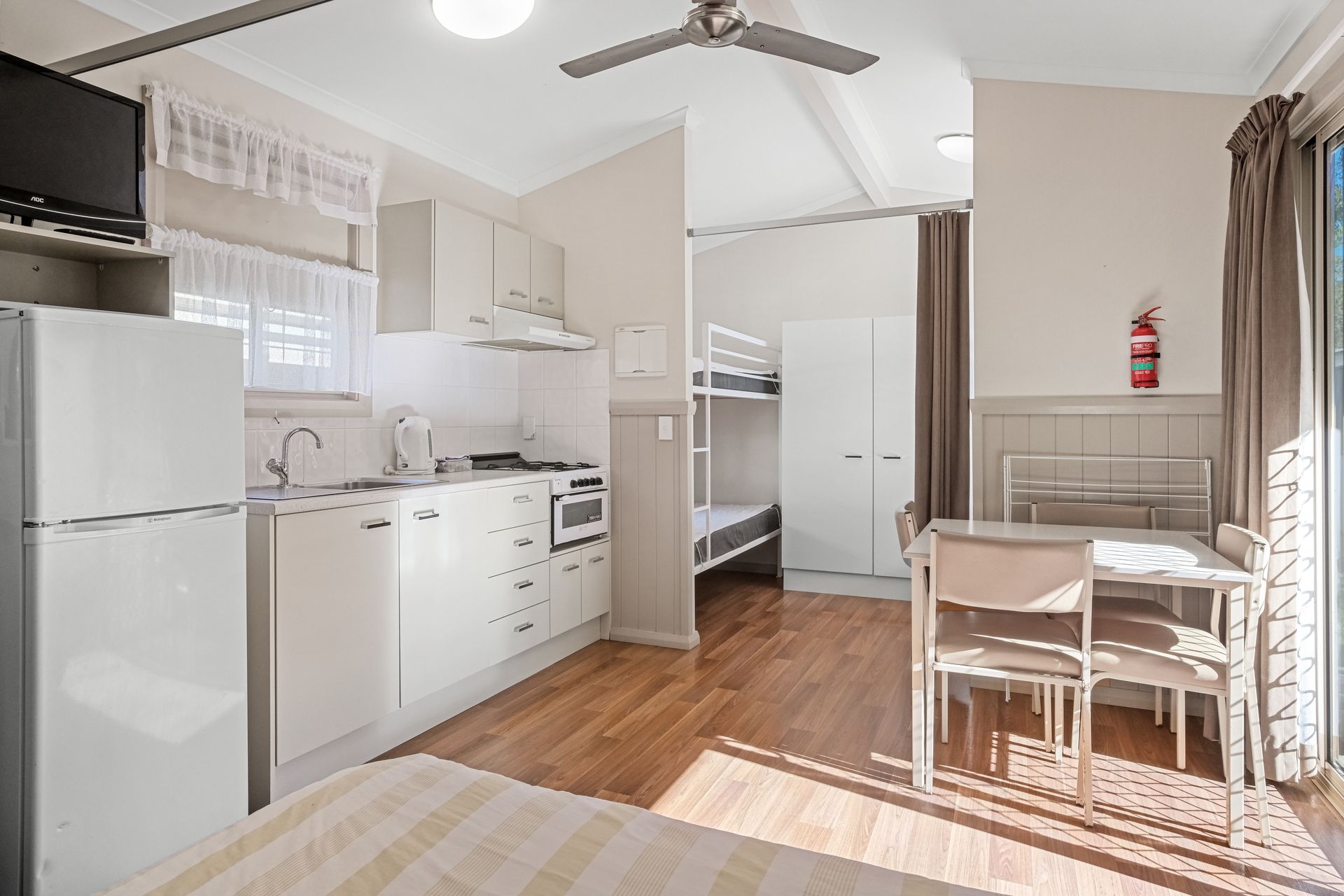 Small Apartment Kitchen With Bunk Beds in the Background and Dining Area, Wooden Floors and Sliding Door — Pacific Palms Caravan Park in Elizabeth Beach, NSW