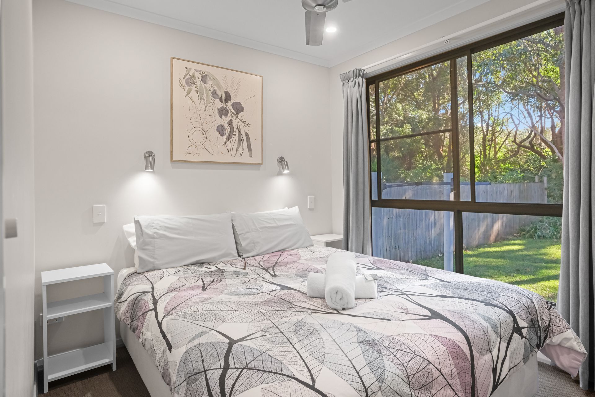 Bedroom with a bed, nightstand, artwork, window with a view of greenery.— Pacific Palms Caravan Park in Elizabeth Beach, NSW