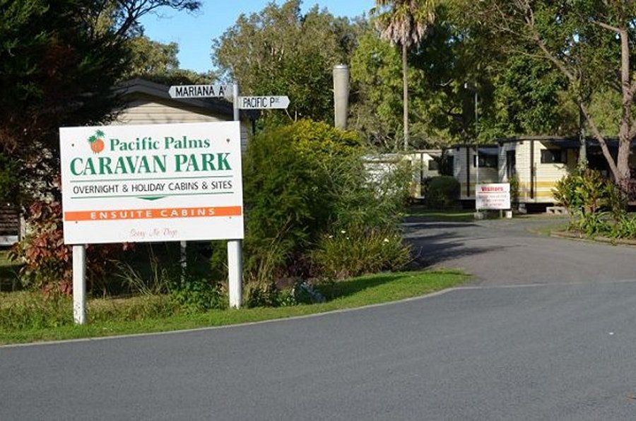 Pacific Palms Caravan Park entrance sign with cabins visible.— Pacific Palms Caravan Park in Elizabeth Beach, NSW