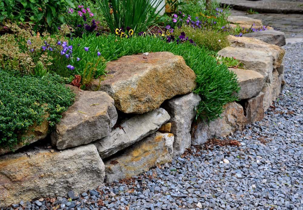 A Rock Wall Surrounded By Gravel And Flowers In A Garden — Mascrete Pty Ltd In Hermit Park, QLD