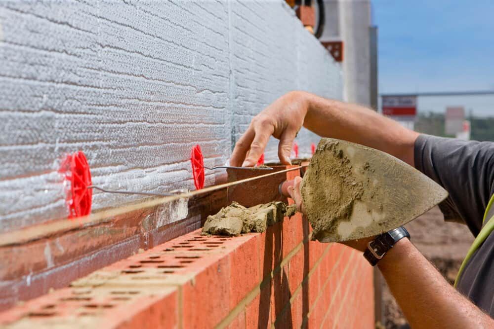 A Man Is Laying Bricks On A Wall With A Trowel — Mascrete Pty Ltd In Hermit Park, QLD