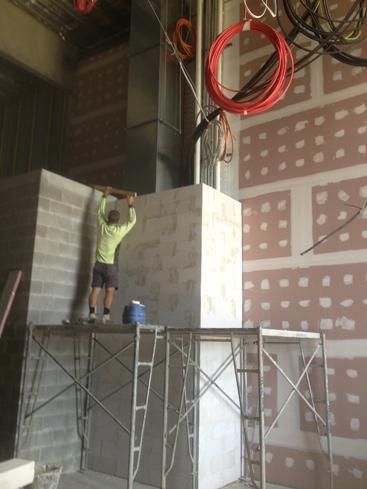 A Man Is Standing On A Scaffolding Working On A Wall — Mascrete Pty Ltd In Hermit Park, QLD