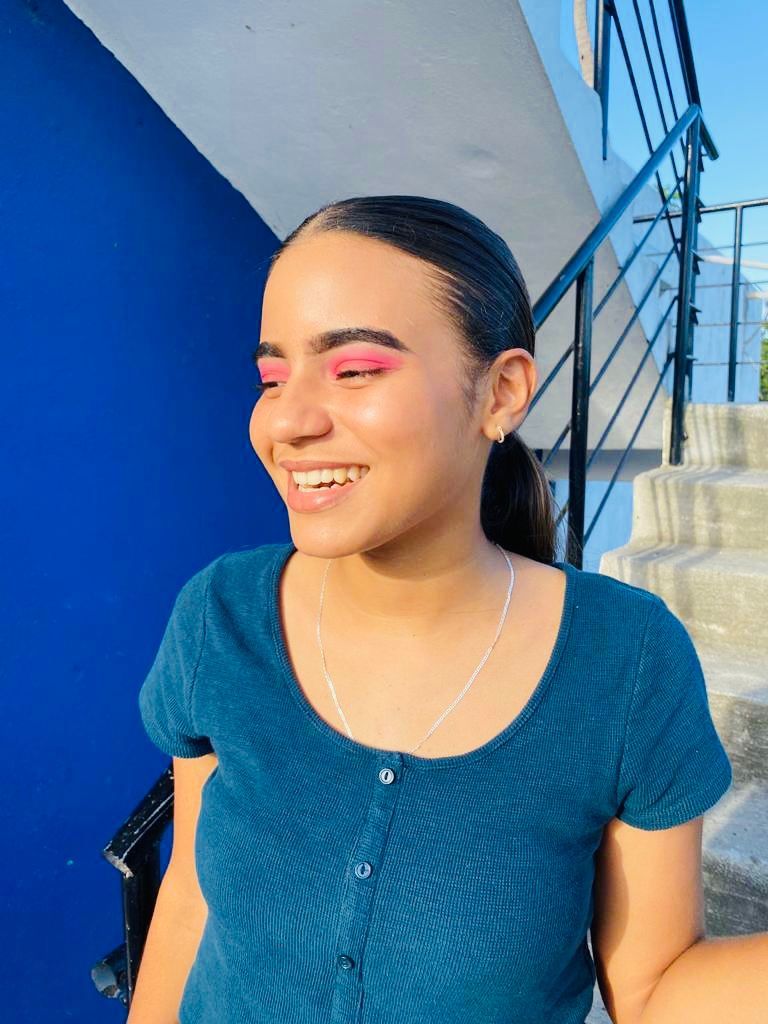A woman wearing pink eye shadow and a blue shirt is smiling.