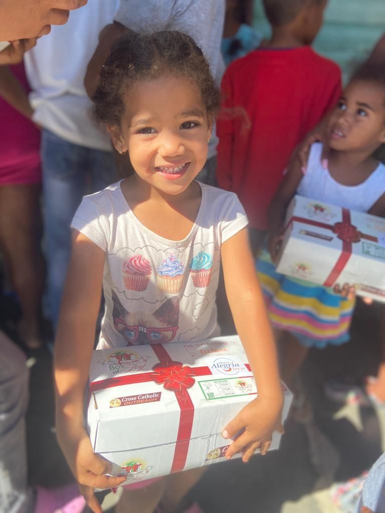A little girl is holding a box with a red ribbon around it.