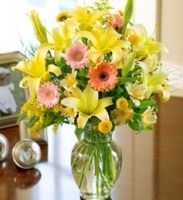 Colorful bouquet of yellow lilies, pink daisies, and greenery in a glass vase on a table