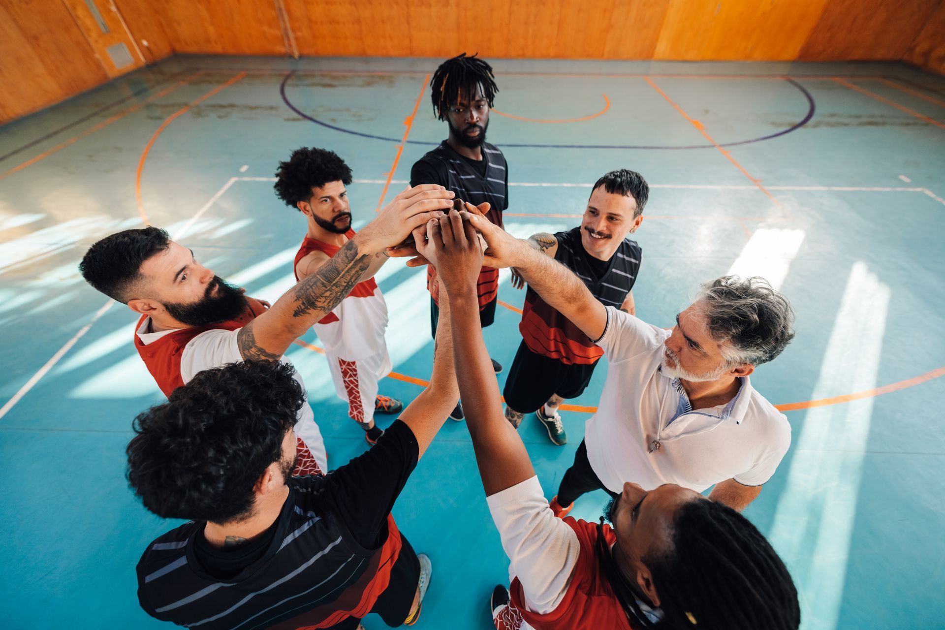 Team of players huddling, arms raised in a circle, on a basketball court.