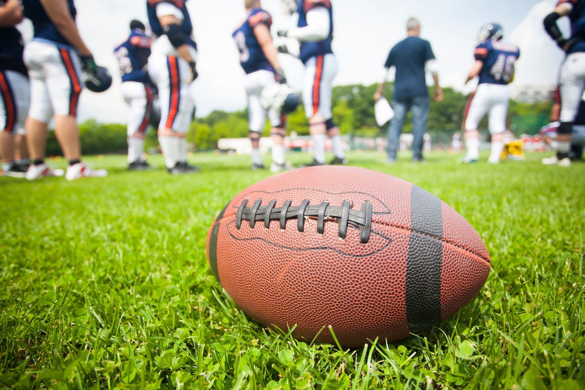 Football on green grass, football players in background.
