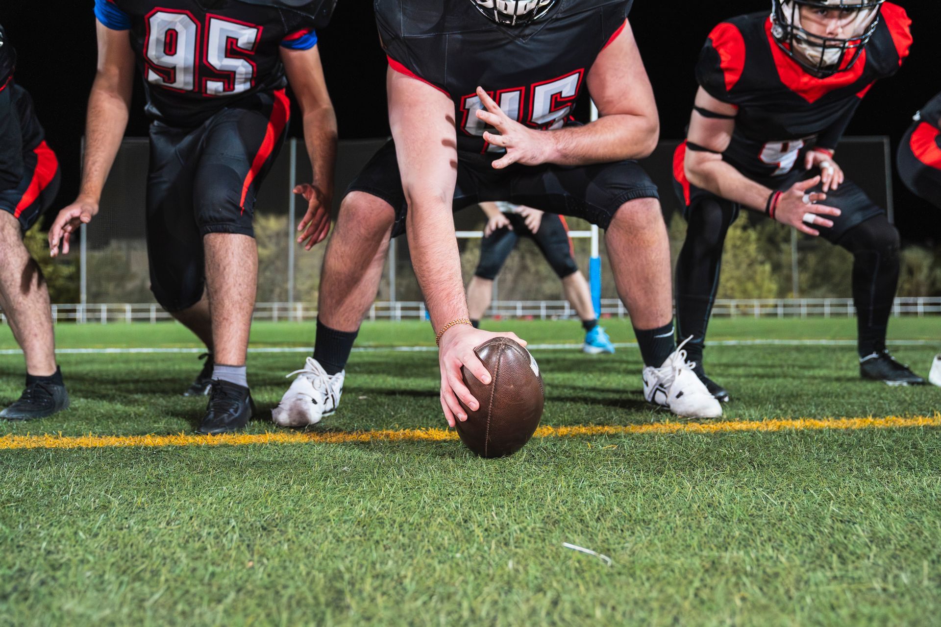 Football players in black and red uniforms line up on a green field, preparing to play.