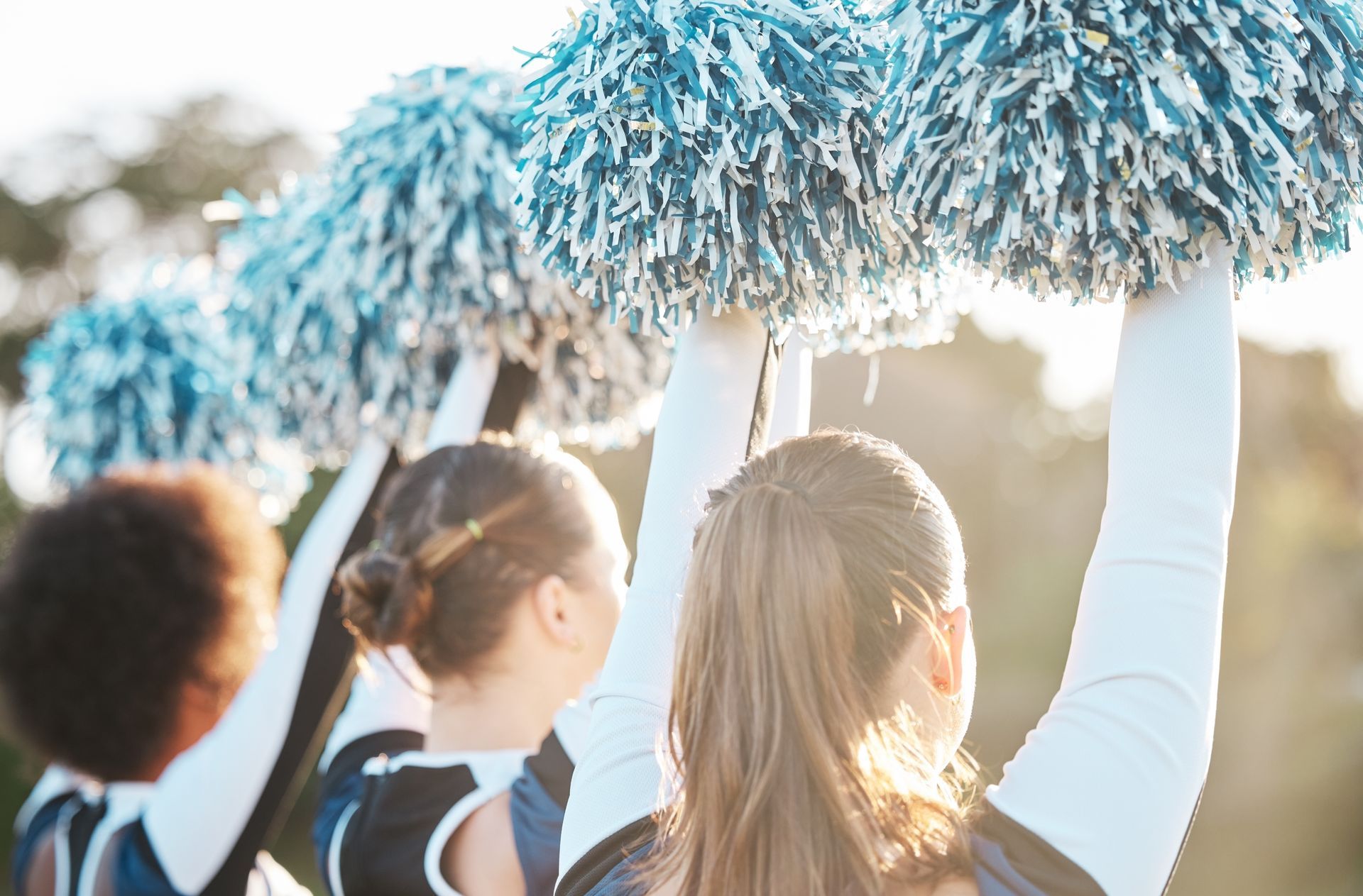 Cheerleaders holding up blue and white pom-poms, arms raised.