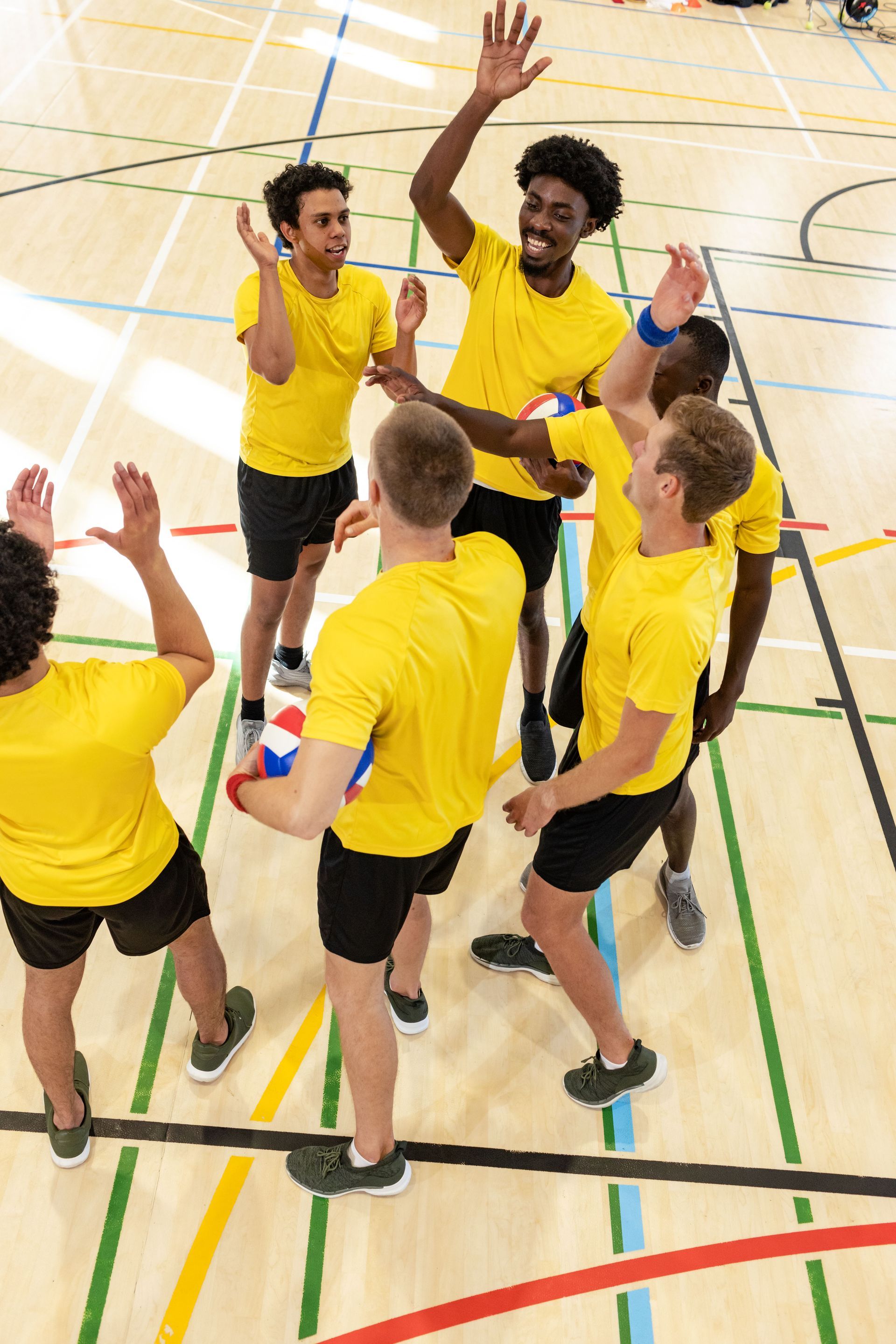 Volleyball team in yellow shirts and black shorts celebrate a point, high-fiving in a gymnasium.