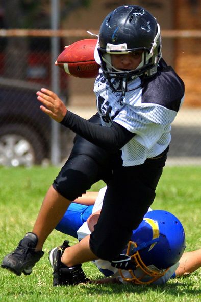 Football player running with ball, being tackled on a green field.