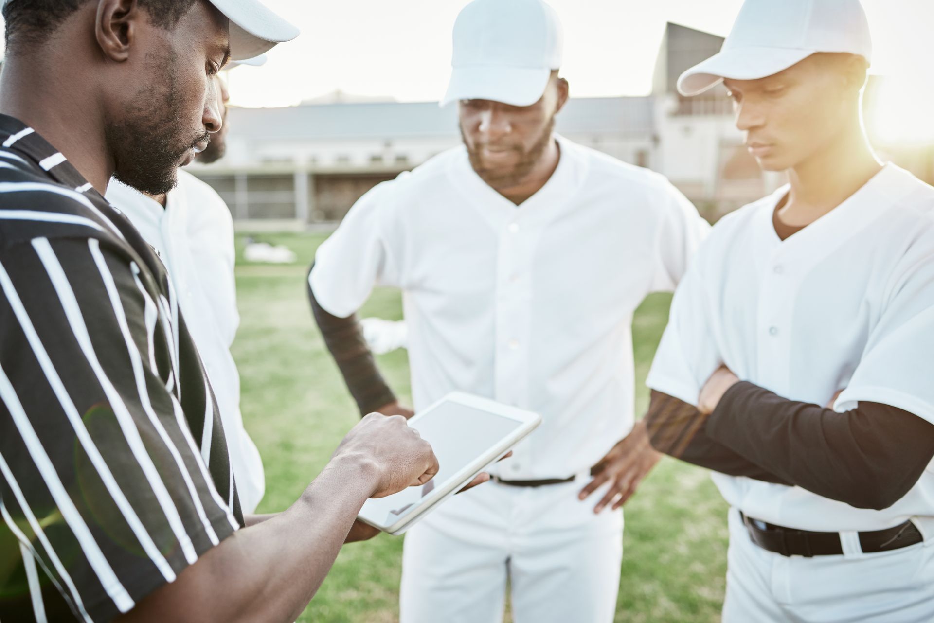 Baseball coach showing a tablet to three players on a field.