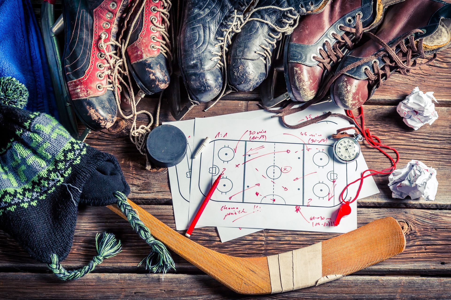 Hockey equipment laid out on a wooden surface, including skates, a diagram of the rink, hat, puck, and stick.