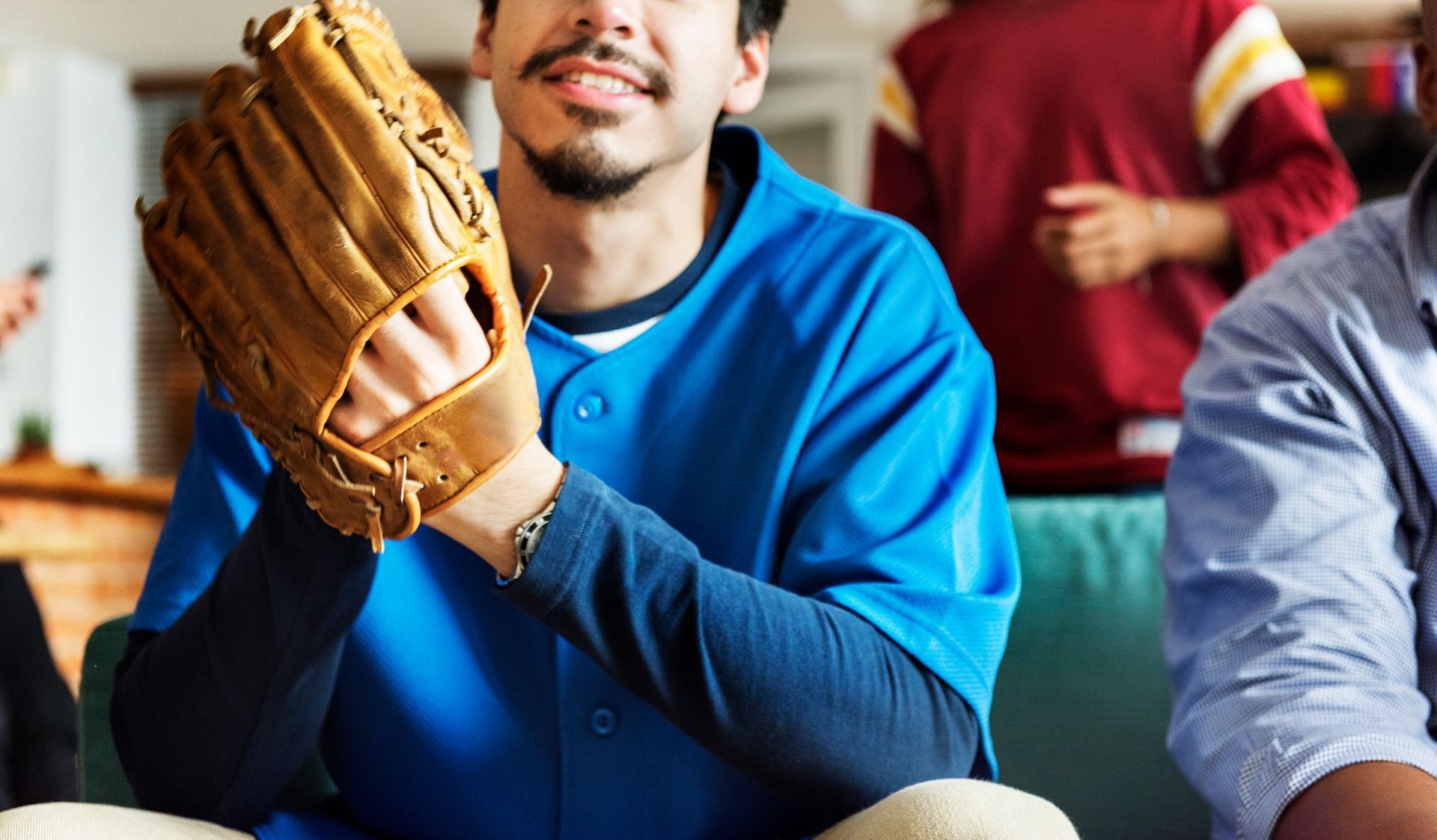 Man in blue baseball jersey holding a baseball glove, smiling.