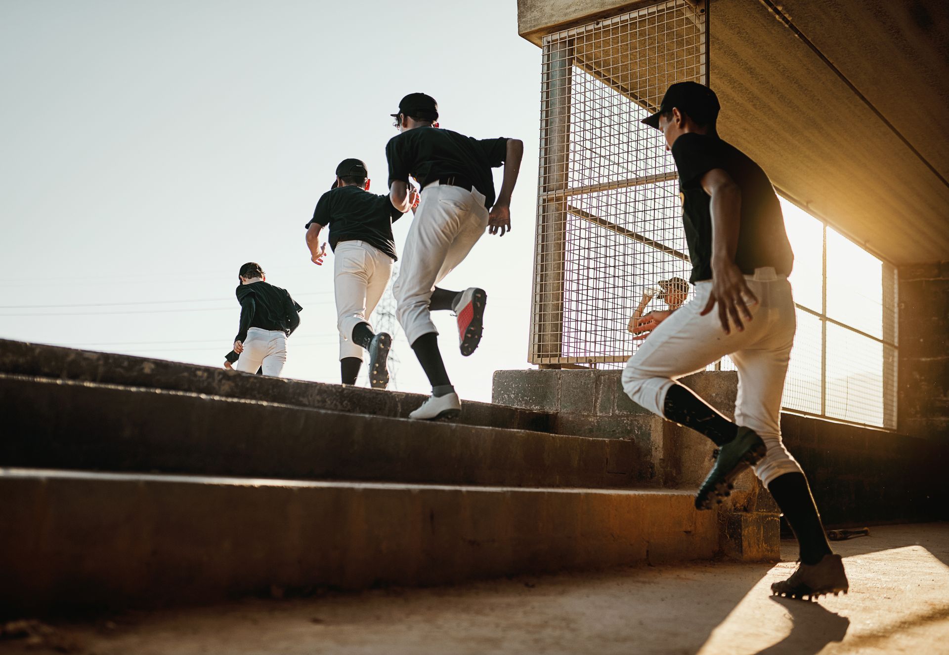 Baseball players in uniform running up concrete stairs in sunlight.