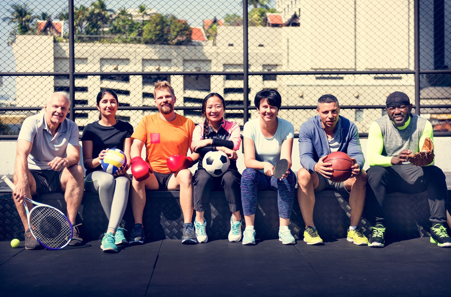 Group of people of varying skin tones holding sports equipment, sitting outdoors smiling.