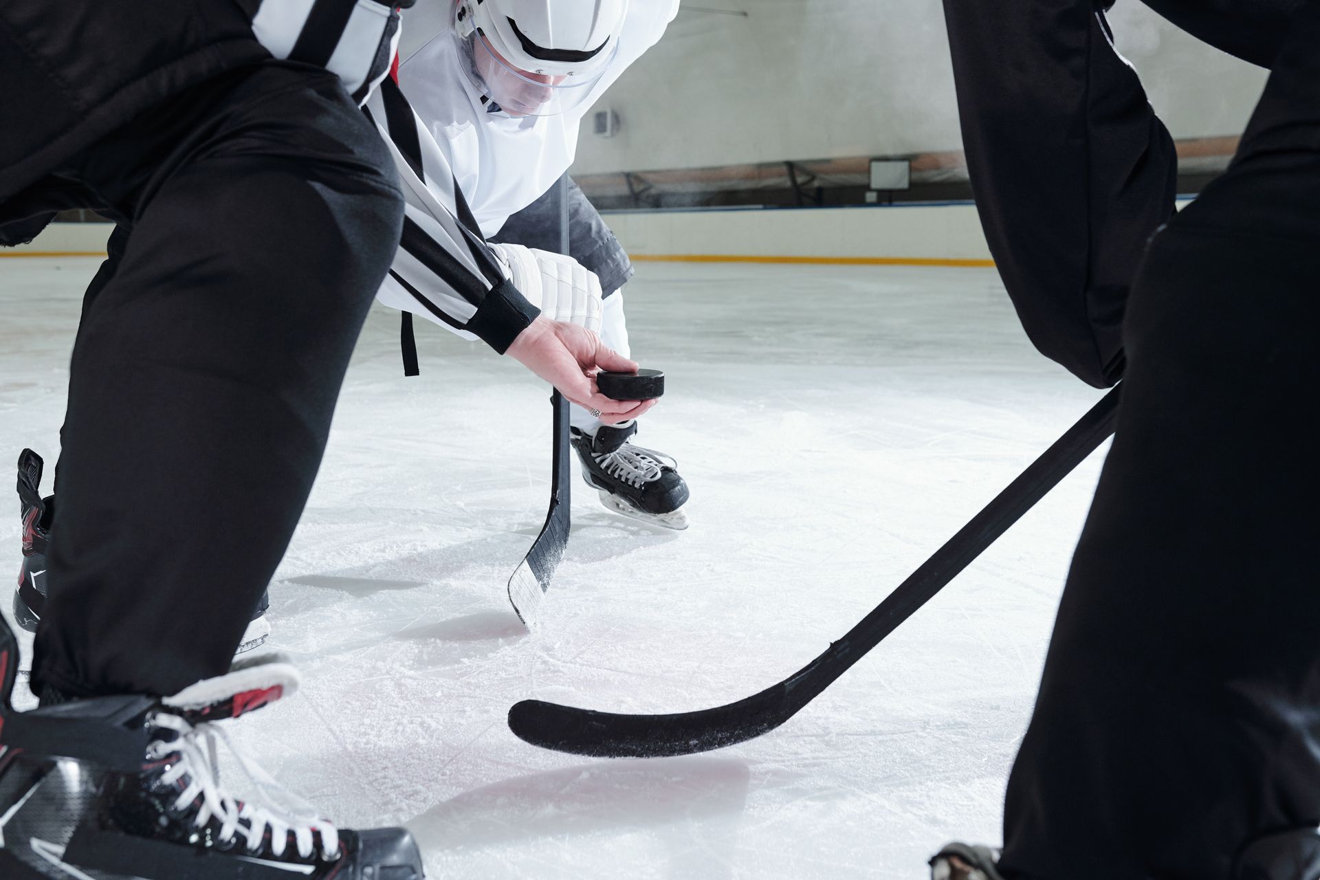 Hockey players face off on ice, referee drops puck.