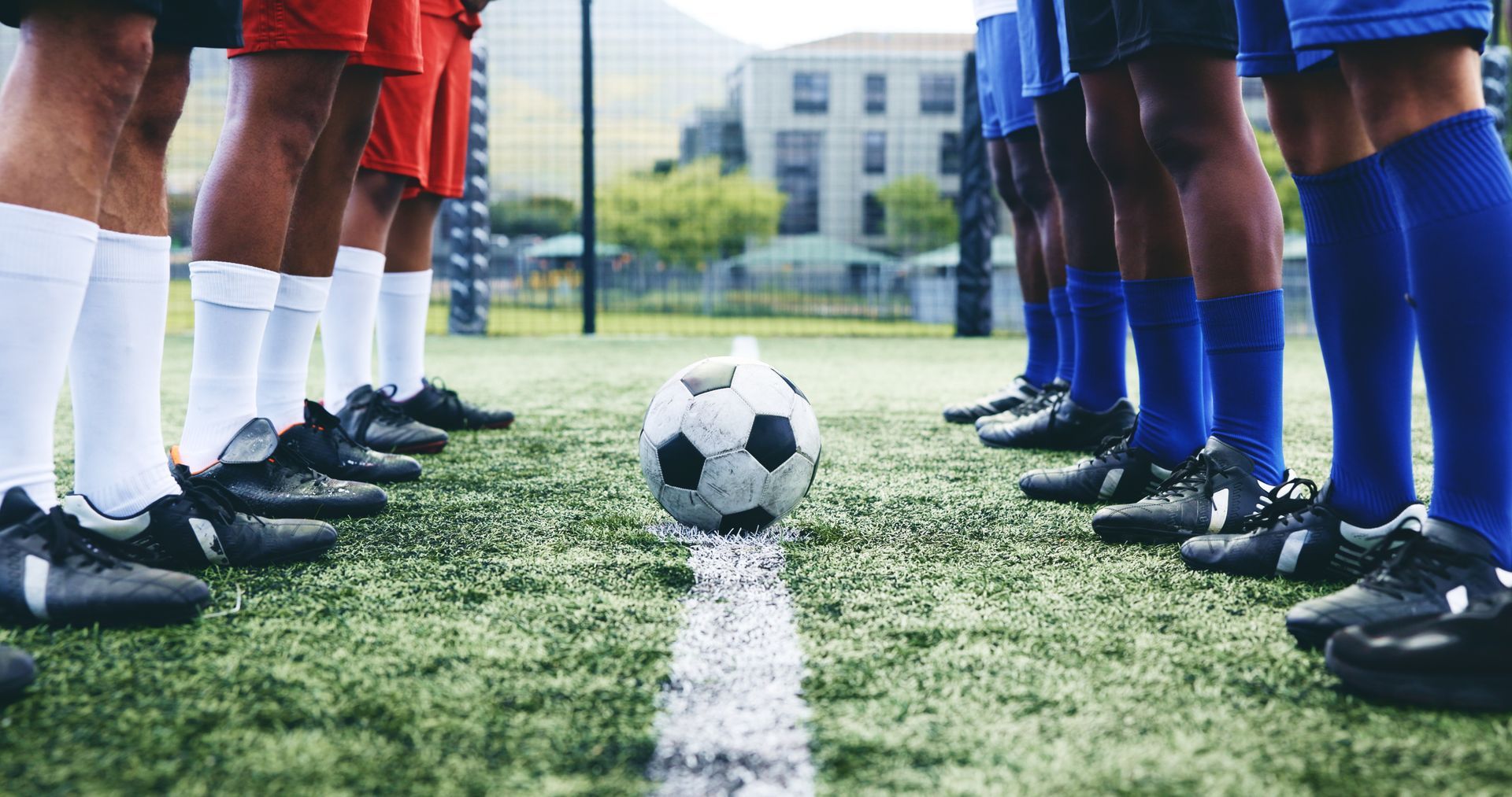Soccer players in red and blue uniforms facing each other on a green field, ball in the center.