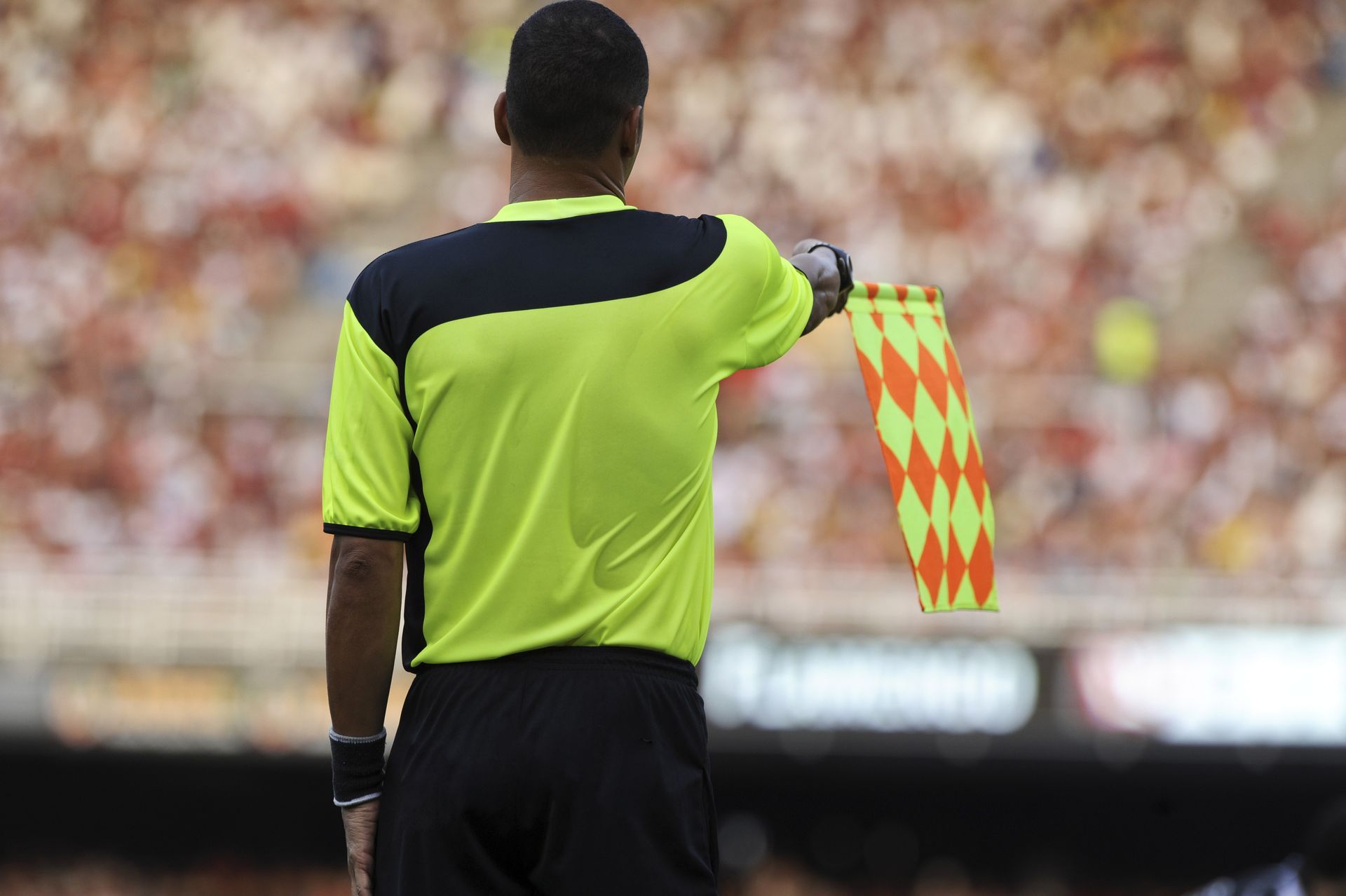Soccer referee with raised flag, signaling offside during a match.