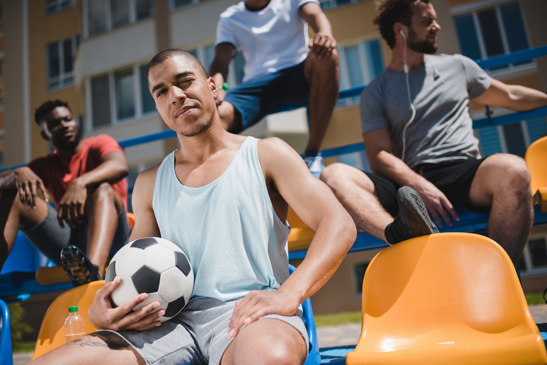 Man holding soccer ball on bleachers with other people.