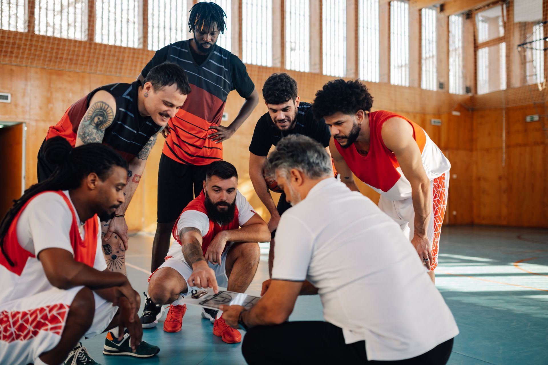 Basketball team and coach huddled on the court, reviewing a tablet.