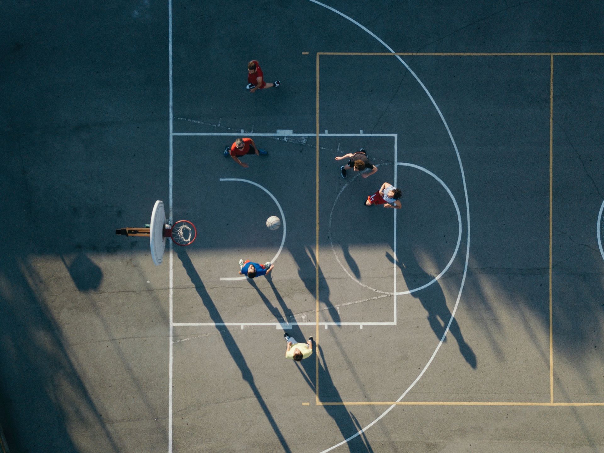 Aerial view of people playing basketball on an outdoor court; ball in play.